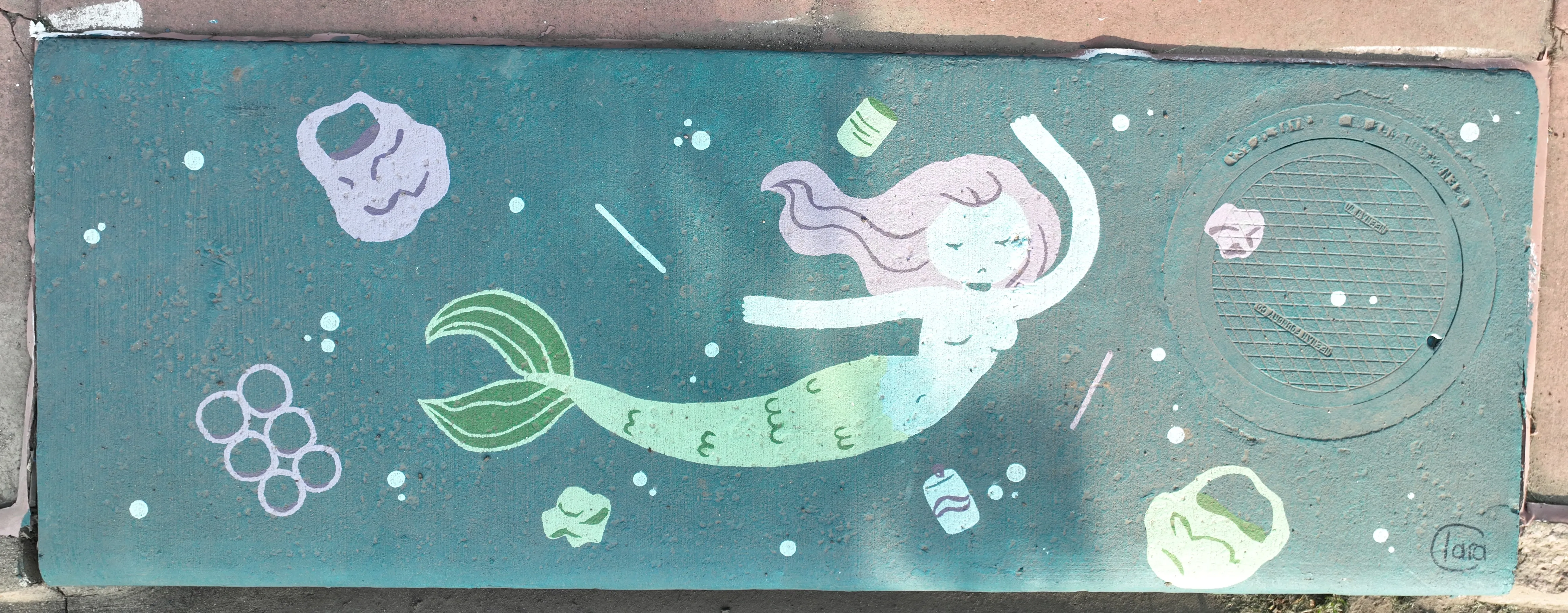 A mural on a storm inlet drain featuring a mermaid in green/blue water surrounded by plastic trash.