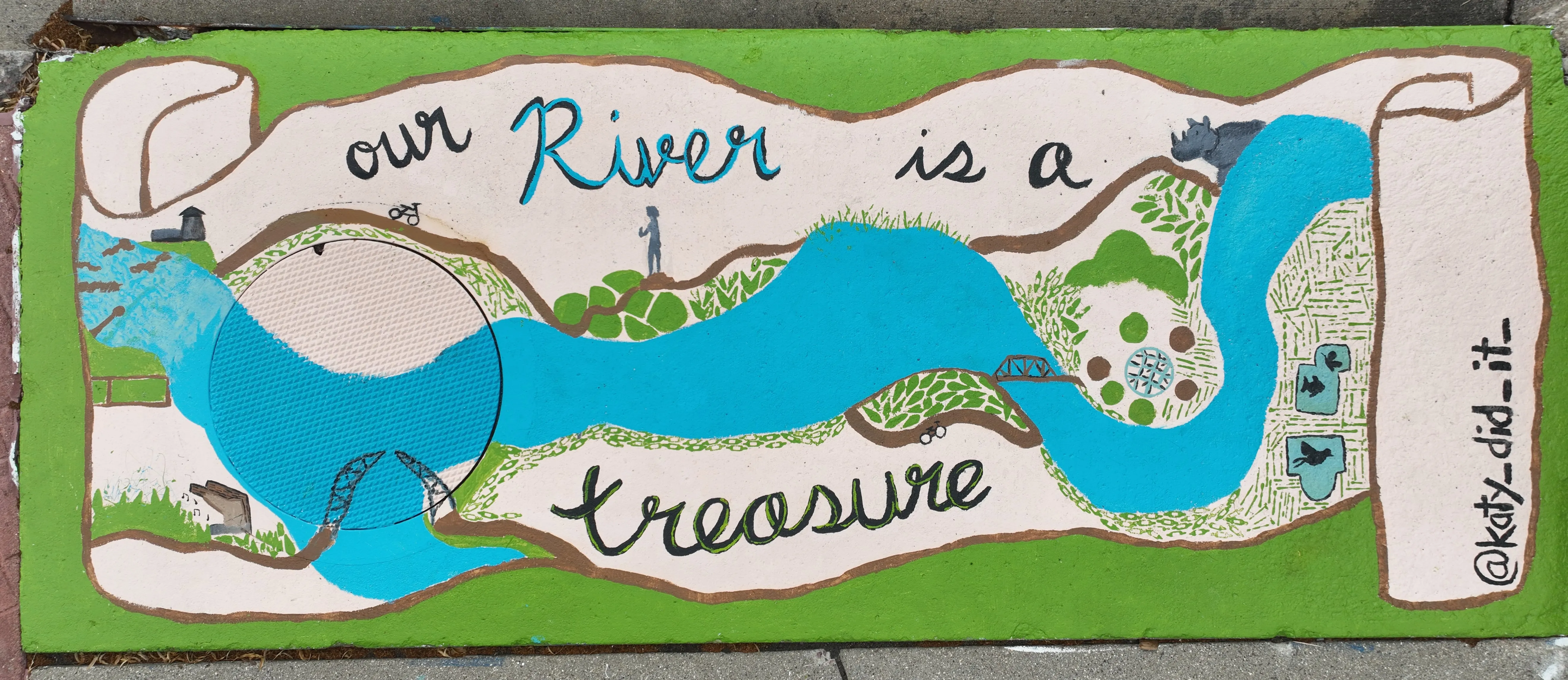 A mural on a storm inlet drain depicting a long rolled map with a river following its length. Sioux Falls landmarks are scattered throughout the map. Text reads "Our river is a treasure"