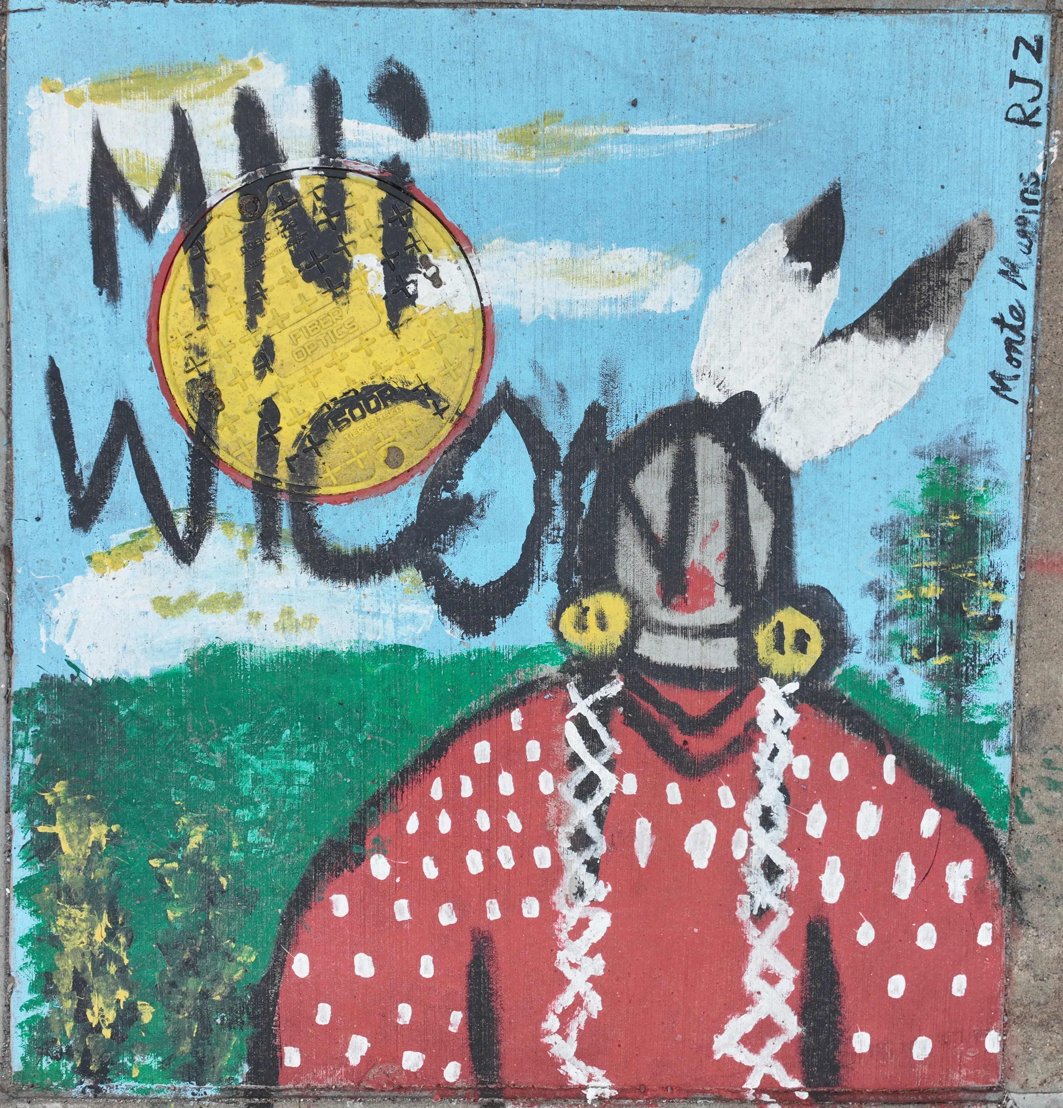A mural on a storm inlet drain depicting a figure with headdress standing in front of a green hill and blue sky. Text reads "Mni Wiconi," or "Water is Life"