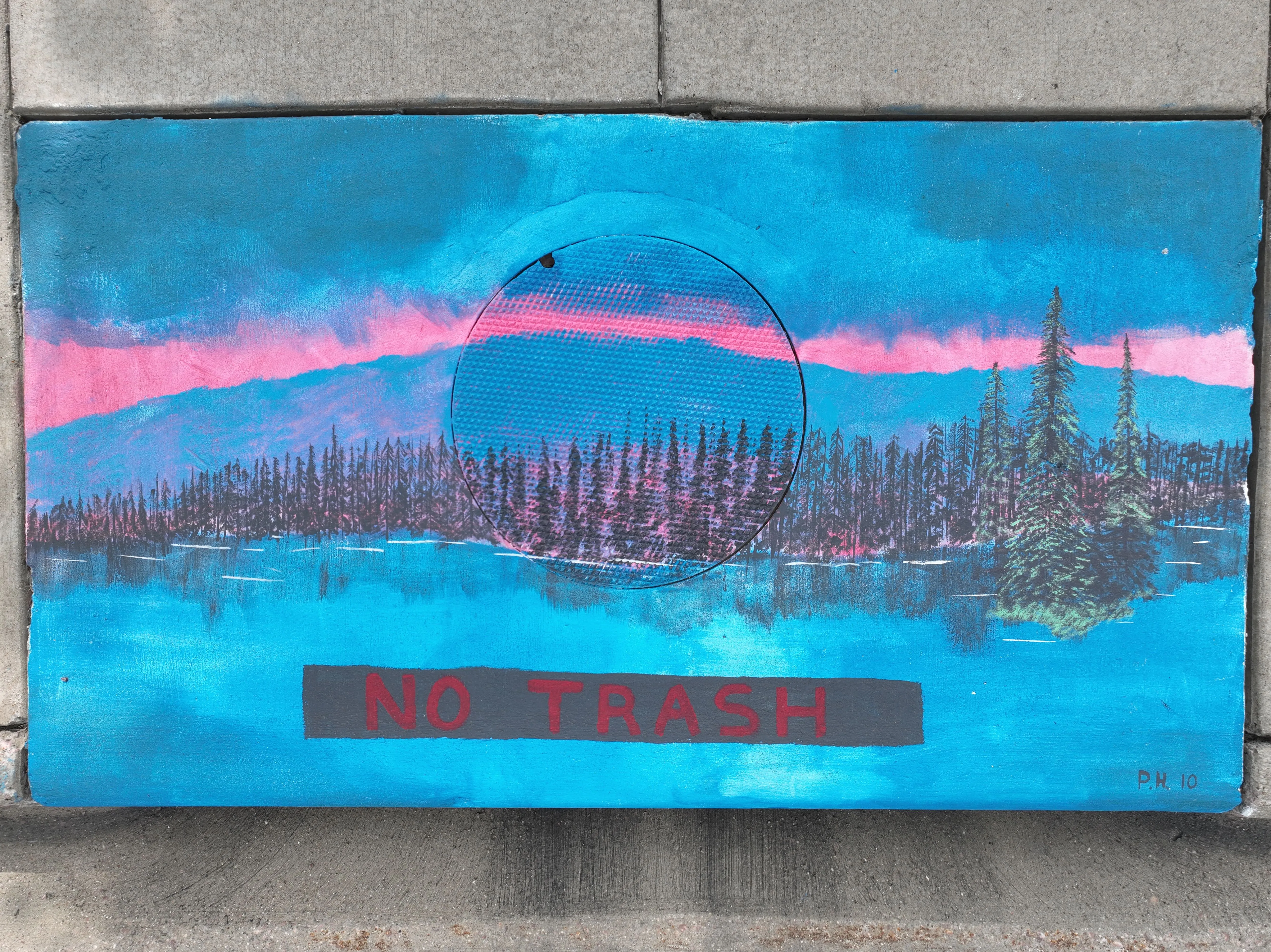 A mural on a storm inlet drain featuring a lake, trees, mountain, and sunset skies, with pink and blue colors. Text reads "No trash"