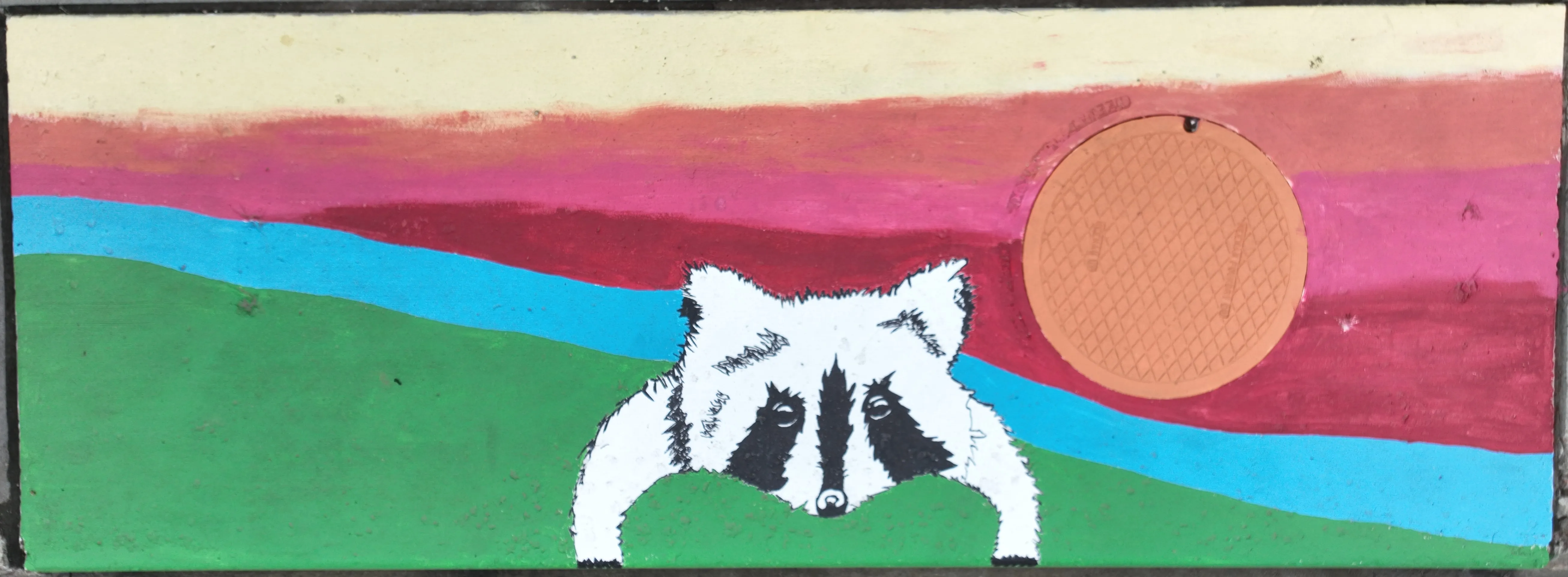 A mural on a stormwater inlet depicting a woodland animal on grass, with a blue river and red/pinkish sun.