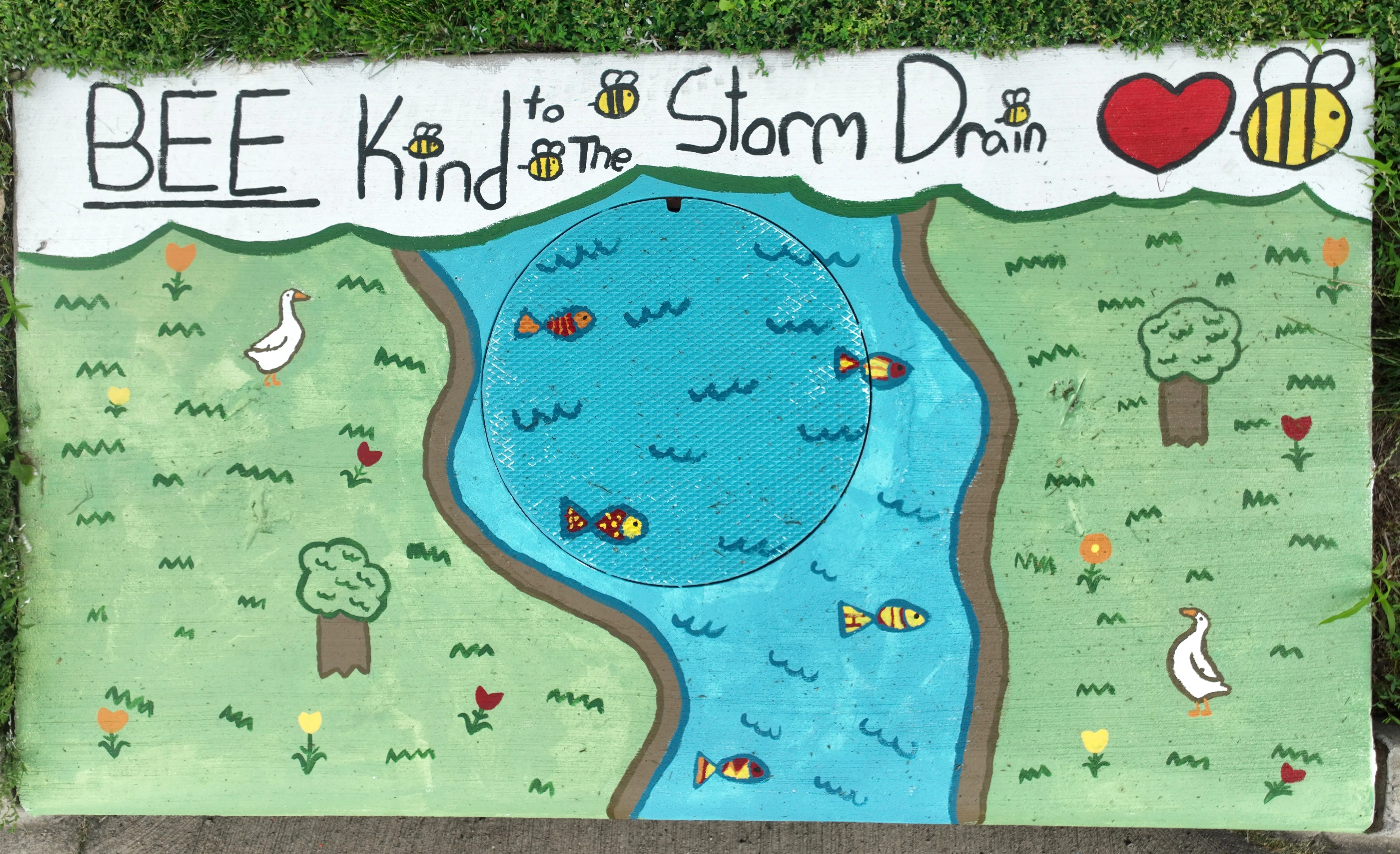 A mural on a storm inlete drain showing a river with fish and surrounded with grass containing geese, flowers, and bees. Text reads "BEE Kind to the Storm Drain"